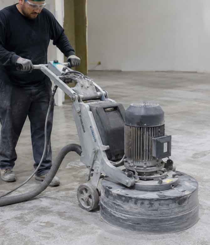 Worker operating a grinder preparing a concrete garage floor for epoxy coatings.
